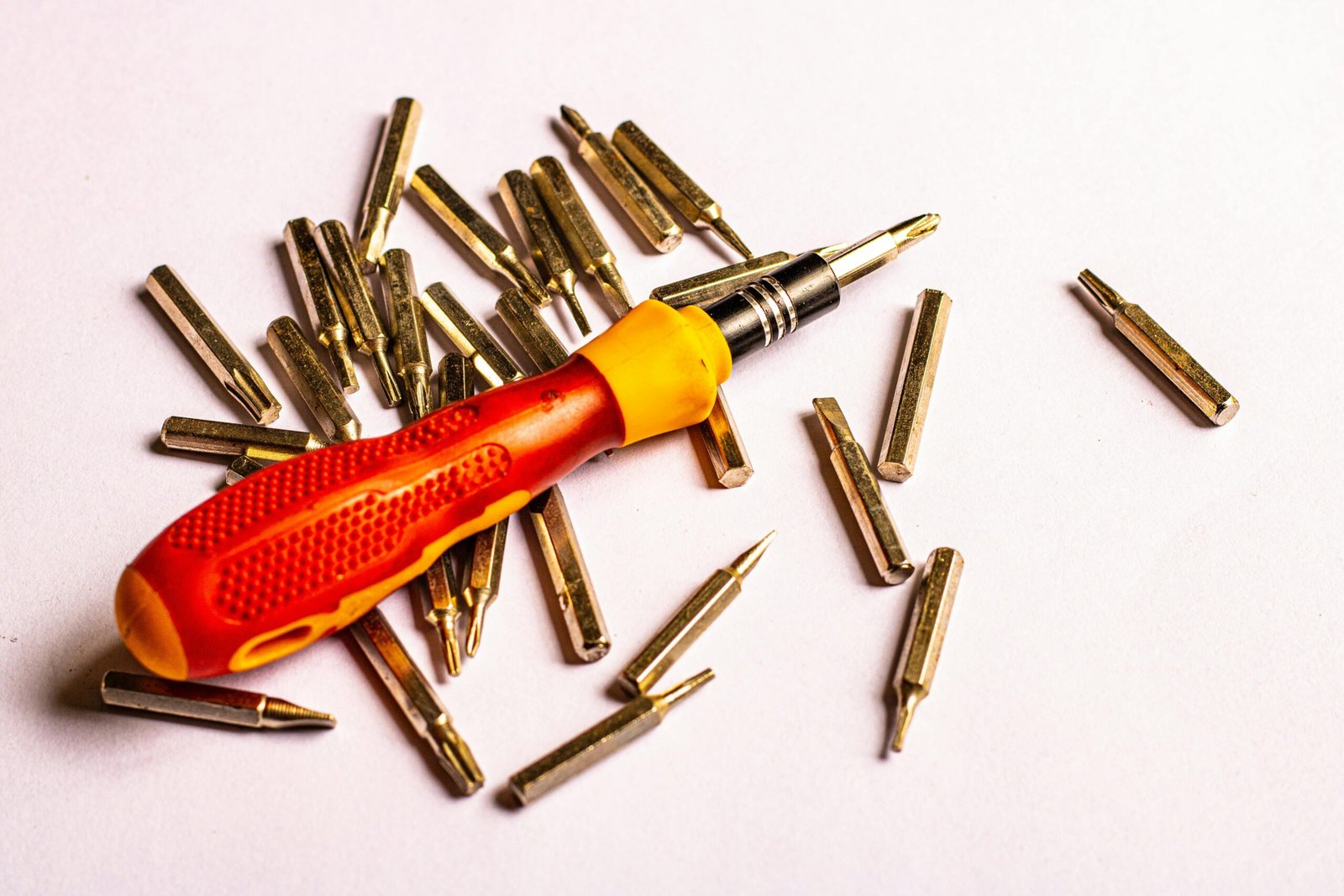 A close-up of a screwdriver with various metal bits on a white background.